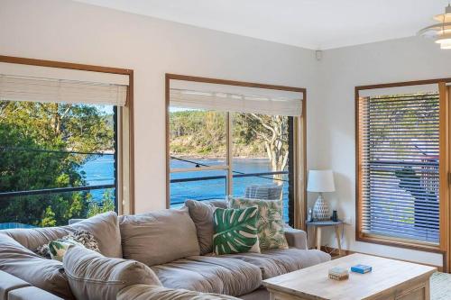 a living room with a couch and two large windows at Gillmith - At the Pambula River Mouth in Pambula Beach