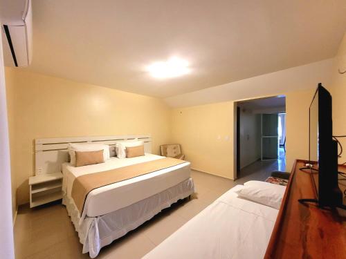 um quarto com uma grande cama branca e uma televisão em Sunset Beach Hotel em Taíba