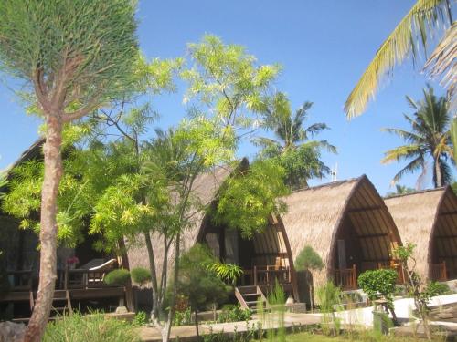 a house with palm trees in front of it at Sandy Beach Bungalows in Gili Islands