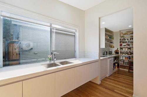 biała kuchnia ze zlewem i oknem w obiekcie Sea Change and Studio on Tasman w mieście Merimbula