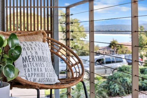 a rattan chair on a balcony with a view of the ocean at Sea Change and Studio on Tasman in Merimbula