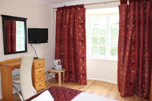 a bedroom with red curtains and a desk and a window at Remarc Guest House in Takeley