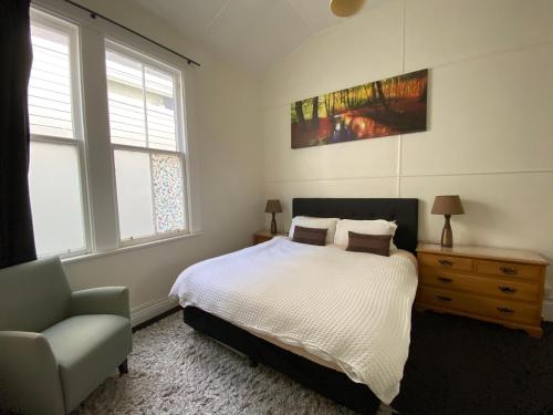 a bedroom with a bed and a chair and two windows at Beach front House in Wellington