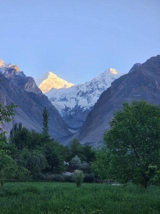 a view of a mountain range with a field and trees at Hunza Lounge in Hunza