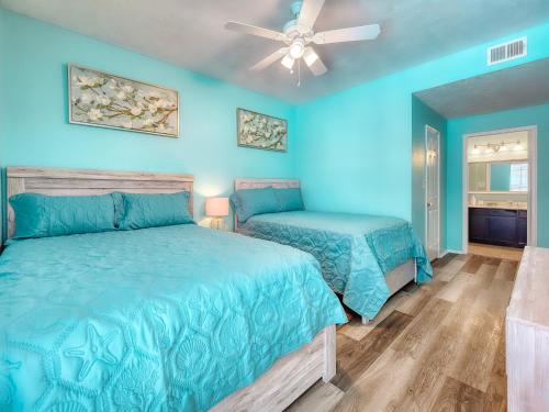 a blue bedroom with two beds and a ceiling fan at NEW!! 2BR 4 Beds Condo with Pool in Galveston