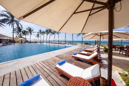a pool with chairs and umbrellas next to the ocean at Victoria Hoi An Beach Resort & Spa in Hoi An