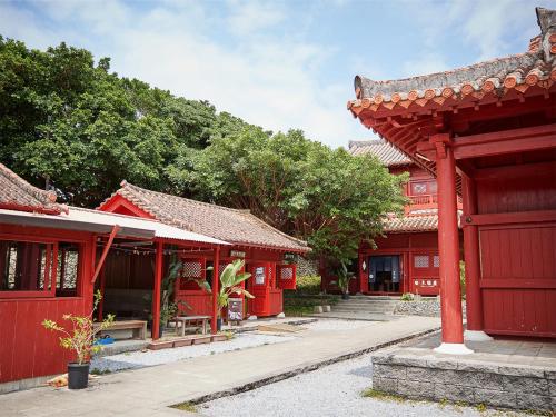 a row of red buildings with trees in the background at Hotel Murasakimura in Yomitan