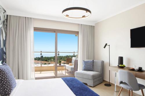 a hotel room with a bed and a chair and a window at Ajul Luxury Hotel & Spa Resort, a Registry Collection Hotel in Agia Paraskevi