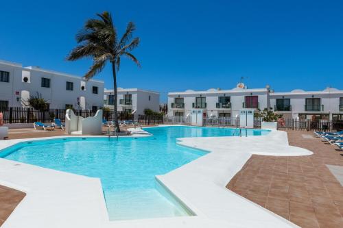 a swimming pool with a palm tree and buildings at Apartamento San Valentin in Corralejo