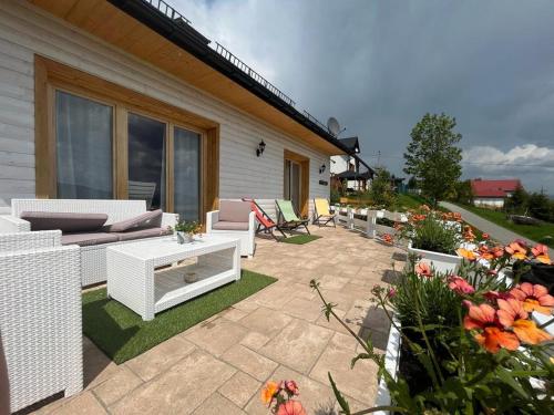 a patio with white furniture and flowers in front of a house at Dom pod kogutem in Laliki