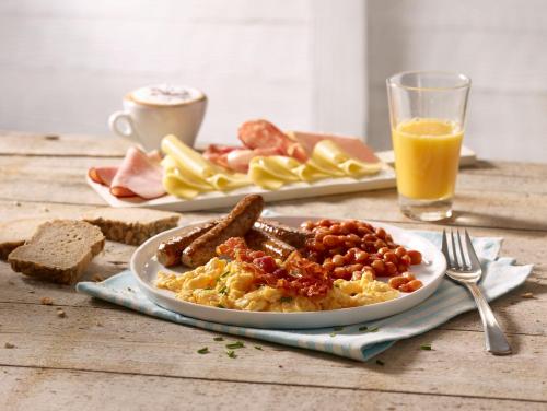 a plate of scrambled eggs with sausage and beans and a glass of orange juice at Premier Inn Saarbrücken City Congresshalle in Saarbrücken