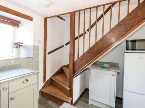 une cuisine avec des placards blancs et un escalier en bois dans l'établissement Tiddlers Cottage, à Bridport