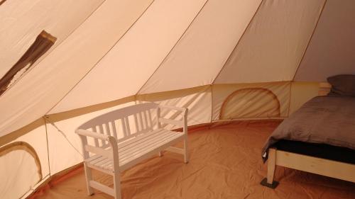 a white bench in a tent with a bed at Cosy Farmhouse Glamping in Stege