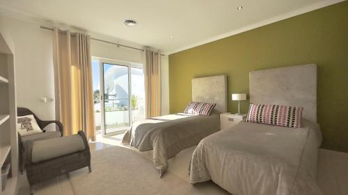 een slaapkamer met twee bedden en een stoel en een raam bij Burgau Sea View, Beach & Pool Villa in Budens