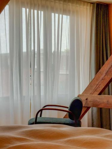 a bed with a chair in front of a window at Boutique Hotel Marie Marie in Dendermonde