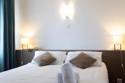a bed with white sheets and pillows and two lamps at Hôtel Les Lentisques in Cargèse