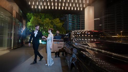 un hombre y una mujer de pie junto a un coche en Kingdom Hotel, en Yiwu