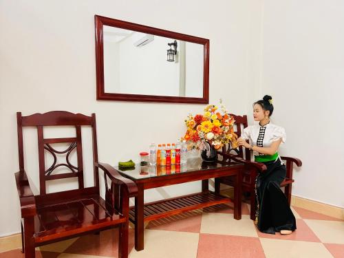 Eine Frau, die an einem Tisch mit einer Blumenvase sitzt. in der Unterkunft Nhà nghỉ Xuân Long - Xuan Long gues - Tỉnh Điện Biên in Ban Hin Lom