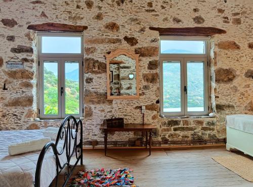 Casa Pappadiana Traditional stonehouse في Kefálion: غرفة نوم بحائط حجري مع نوافذ وطاولة
