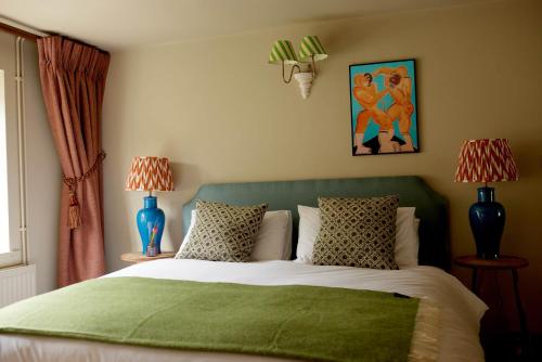 a bedroom with a bed with a green headboard and two lamps at The Queen's Head in Broad Chalke