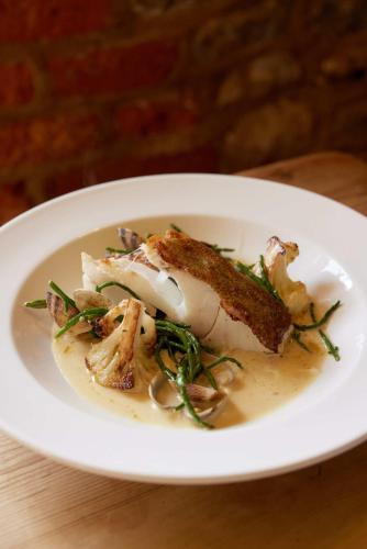 a white plate of food with a piece of fish at The Queen's Head in Broad Chalke