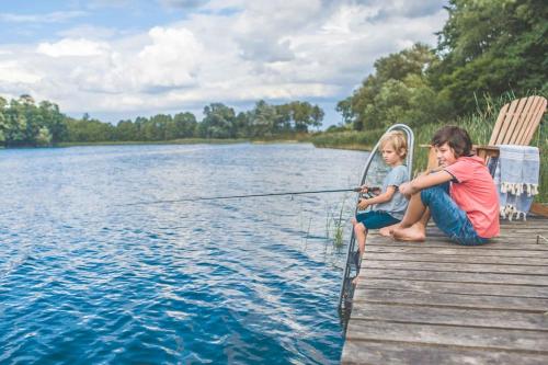 two children sitting on a dock fishing on a lake at Lunette Lodge for 10 guests, 50 m from the lake, sauna, hot tube in Brzozie