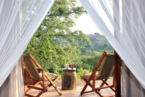 two chairs and a table on a porch with a view at Big Cave Camp in Matopos