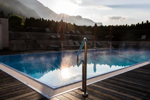 ein Pool mit der Sonne, die im Wasser reflektiert in der Unterkunft KUHOTEL by Rilano in Waidring