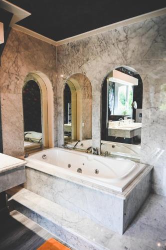 une grande salle de bain avec une baignoire et un grand miroir dans l'établissement La Fontaine Dort, à Tessy-sur-Vire