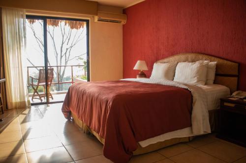 a bedroom with a bed with a red wall and a window at Camino Real Tikal‎ in El Remate