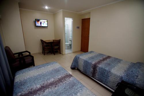 a bedroom with two beds and a table and a television at Hotel America do Sul in Sao Paulo