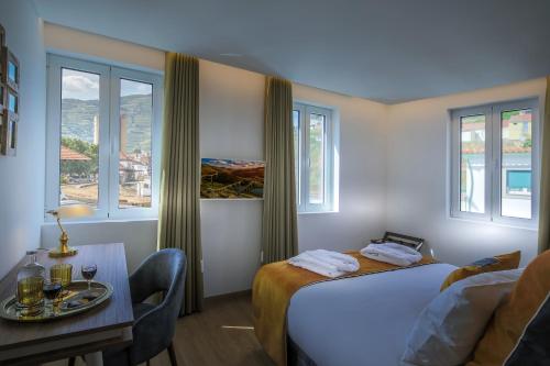 a hotel room with a bed and a table and windows at A Tendinha - Guest House in Peso da Régua