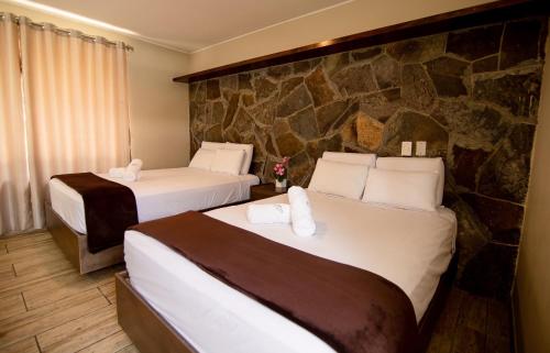 Habitación de hotel con 2 camas y pared de piedra. en Hotel Campo & Leña, en Cieneguilla