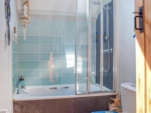 a bathroom with a tub and a shower with blue tiles at Puffin Cottage in Abereiddy