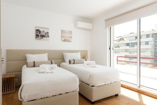 two beds in a white room with a window at Marina Vilamoura Triplex in Vilamoura