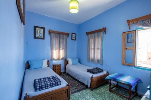 a blue bedroom with two beds and a table at Hotel Asmara in Chefchaouen