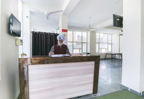 a man with a face mask sitting at a desk at OYO Spring Woods Suites in Sohāna