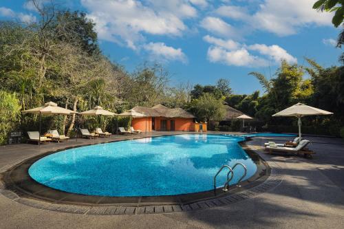 a pool at a resort with chairs and umbrellas at Taj Corbett Resort and Spa Uttarakhand in Rāmnagar