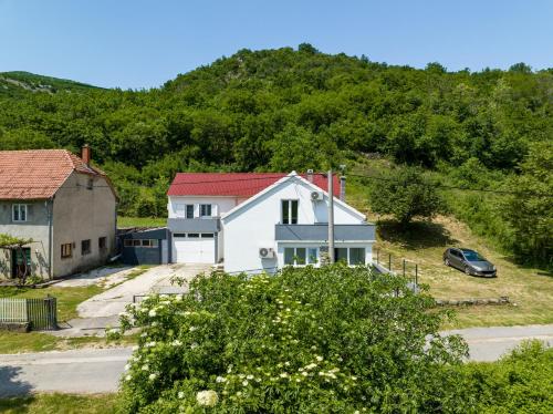 a white house with a red roof in front of a hill at Holiday House Zrmanja Vrelo in Zrmanja Vrelo