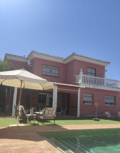 une maison rose avec des chaises, un parasol et une piscine dans l'établissement Villa 28 de julio Casa Rural con piscina en Granada, à Grenade