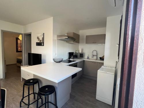 une cuisine avec un comptoir blanc et deux tabourets de bar dans l'établissement Appartement pour 2 personnes en ville avec terrasse, à La Londe-les-Maures