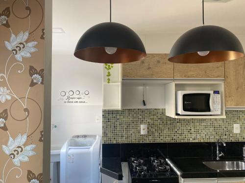a kitchen with two black lamps and a microwave at Hotel APART Zuccolotto 101 in Aracruz