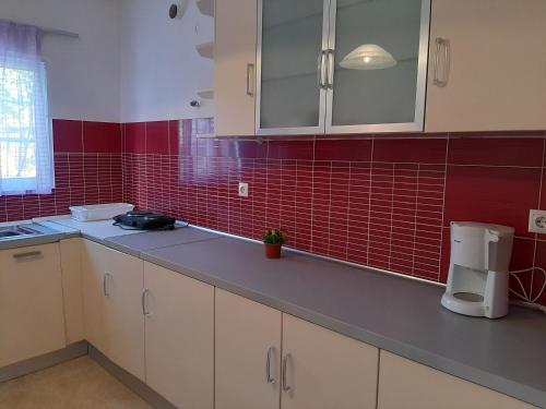 a kitchen with white cabinets and red tiled walls at Cozy flat in Nea Makri in Nea Makri