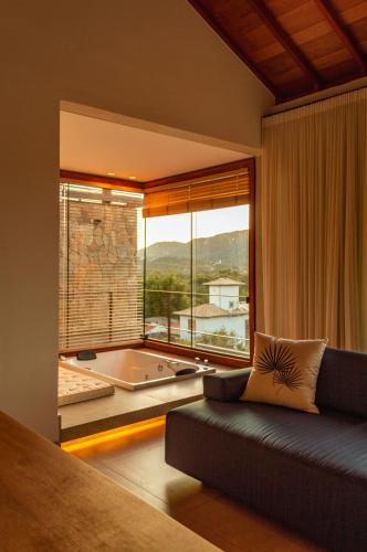 a room with a couch and a large window with a tub at Lofts Villa Gratiam in Tiradentes