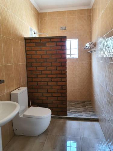 a bathroom with a toilet and a sink and a brick wall at Stream Box Lodge in Lilongwe