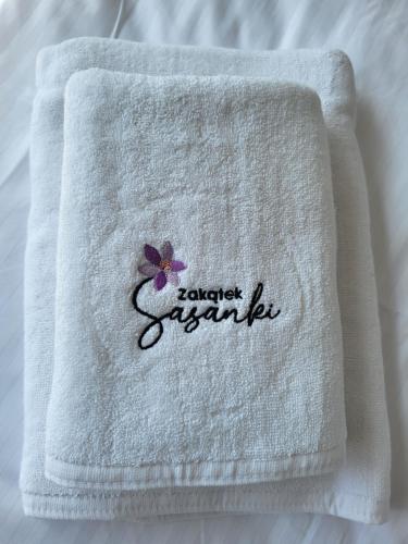 a white towel with a flower on it on a bed at Zakątek Sasanki in Lubiatowo