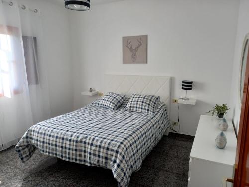 a white bedroom with a bed with a checkered blanket at Casa Caleta Caballo in Caleta de Caballo