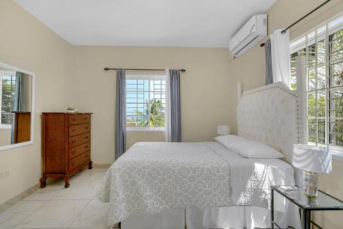 a bedroom with a bed and a dresser and windows at Palm Leaf Cottage in Montego Bay