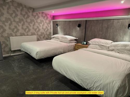 two beds in a hotel room with pink lighting at TheWaterfrontLodges in Coventry