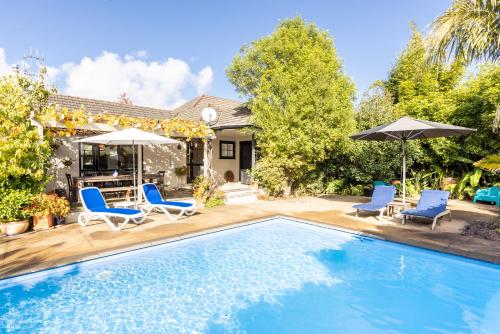 a pool with chairs and umbrellas next to a house at Village Apartment Havelock North in Havelock North